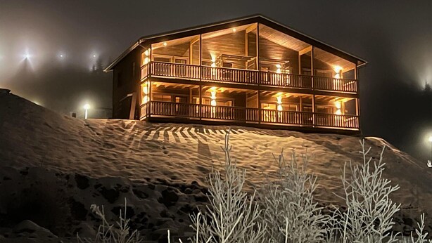 A multi-story wooden cabin with balconies, situated on a snowy slope.
