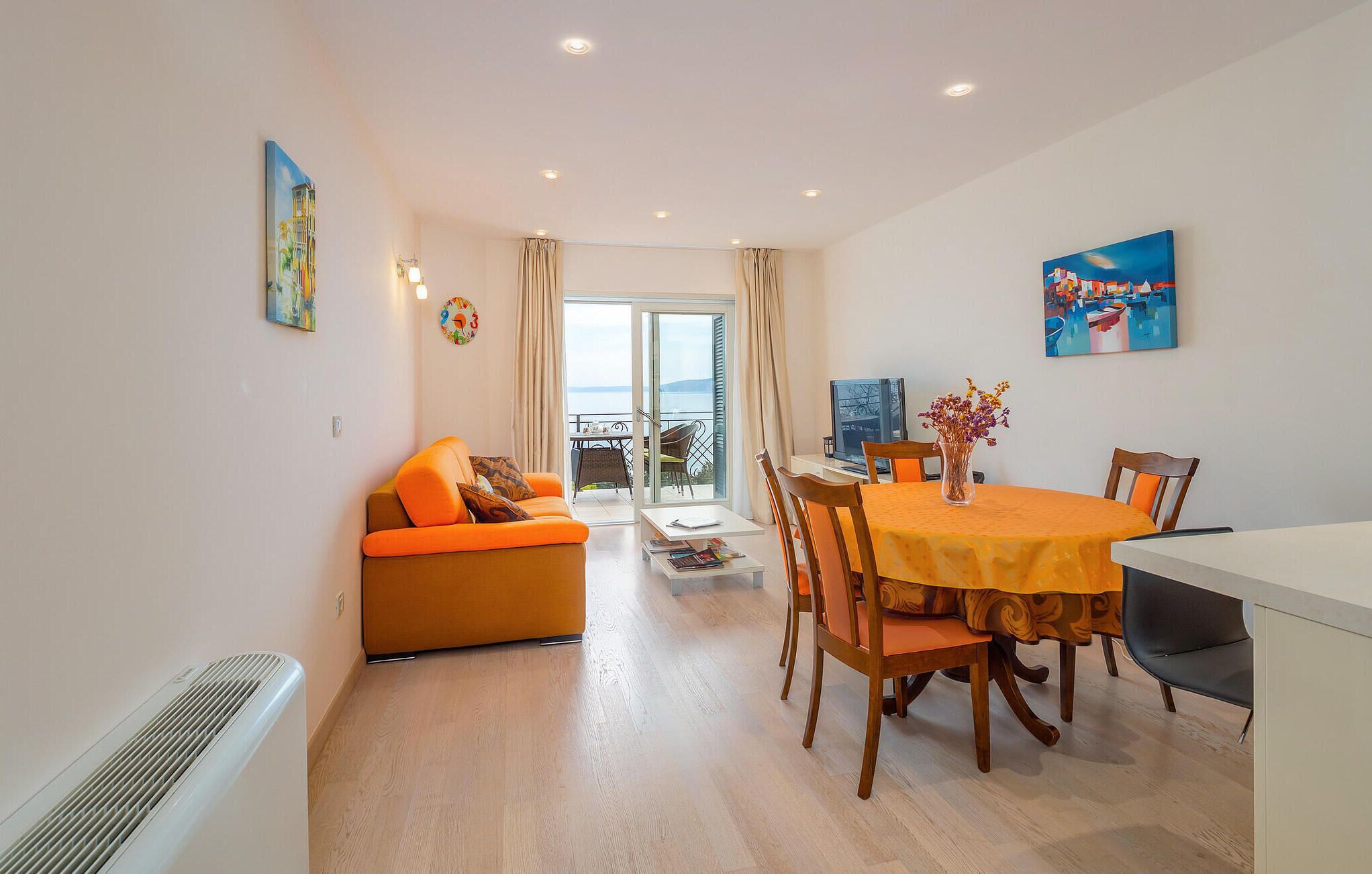 Un salón luminoso con un sofá, una mesa de comedor con sillas y vista al mar a través de un ventanal.