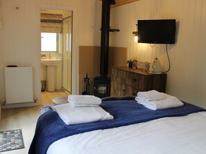 A bedroom with a bed, a dresser, a television, a radiator, and a bathroom visible through an open door. - Otters Crouch (Belford)