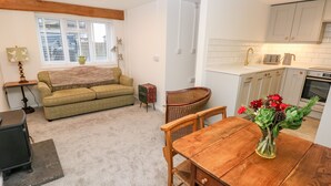 A cozy living room with a green sofa, a wooden dining table with chairs, and a small side table. - Rosemary Cottage (Tenby)
