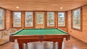Une table de billard dans une pièce aux murs en bois et aux grandes fenêtres.