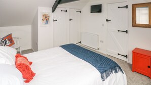 A bedroom with a bed, a red cabinet, a white radiator, and a door with a window. - Clementine Cottage (Tenby)