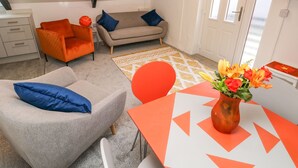A modern living room with a grey sofa, orange armchair, and a small table with a vase of flowers. - Clementine Cottage (Tenby)