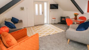 A cozy loft-style living room with a fireplace, a television, and a dining area. - Clementine Cottage (Tenby)