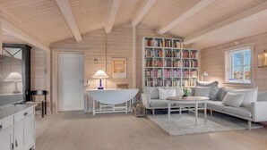 A cozy, well-lit room with a wooden ceiling, a white sofa, a coffee table, a bookshelf filled with books, and a window with a view. - Pet friendly home in Hornbæk with WiFi (Hornbæk)