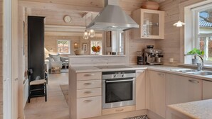 A modern kitchen with wooden cabinetry, a built-in oven, a coffee machine, and a large window providing natural light. - Pet friendly home in Hornbæk with WiFi (Hornbæk)