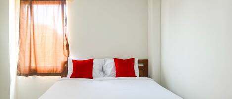 A hotel room with a bed, a window with curtains, an air conditioning unit, and a red carpet.