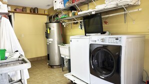 Zona de lavandería con lavadora, secadora y ropa doblada en estantes.