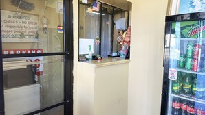 Máquina expendedora con Mountain Dew y otras gaseosas, una ventana con un letrero, y un cartel de estacionamiento.