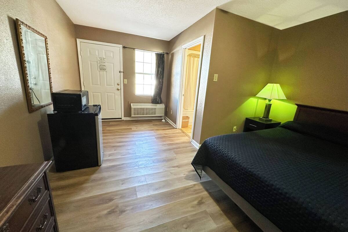A bedroom with a bed, dresser, and a desk with a lamp.