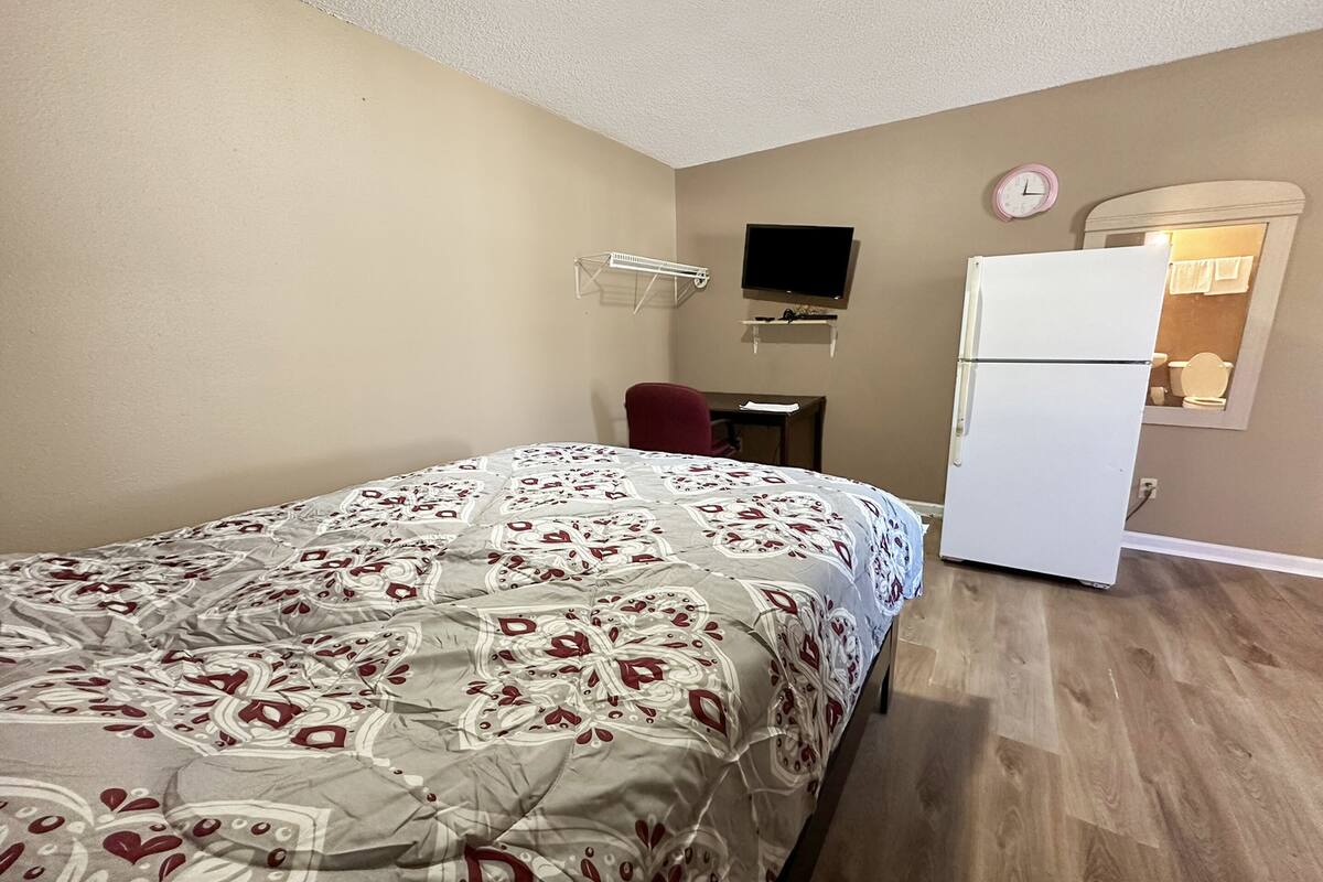 A bedroom with a bed, a desk, a chair, a refrigerator, a television, and a mirror.