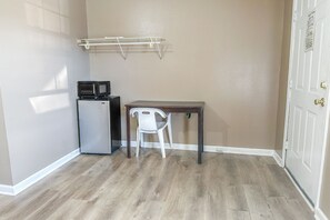 Quarto nos fundos com piso de madeira, uma cadeira branca, uma mesa pequena, micro-ondas e um varal.