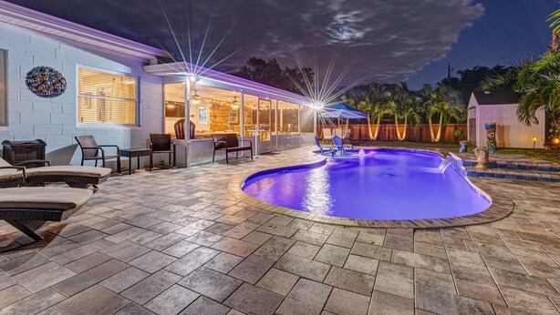 A well-lit outdoor swimming pool area with lounge chairs and a bar. - Brian and Sarahs Hidden Gem (Merritt Island)
