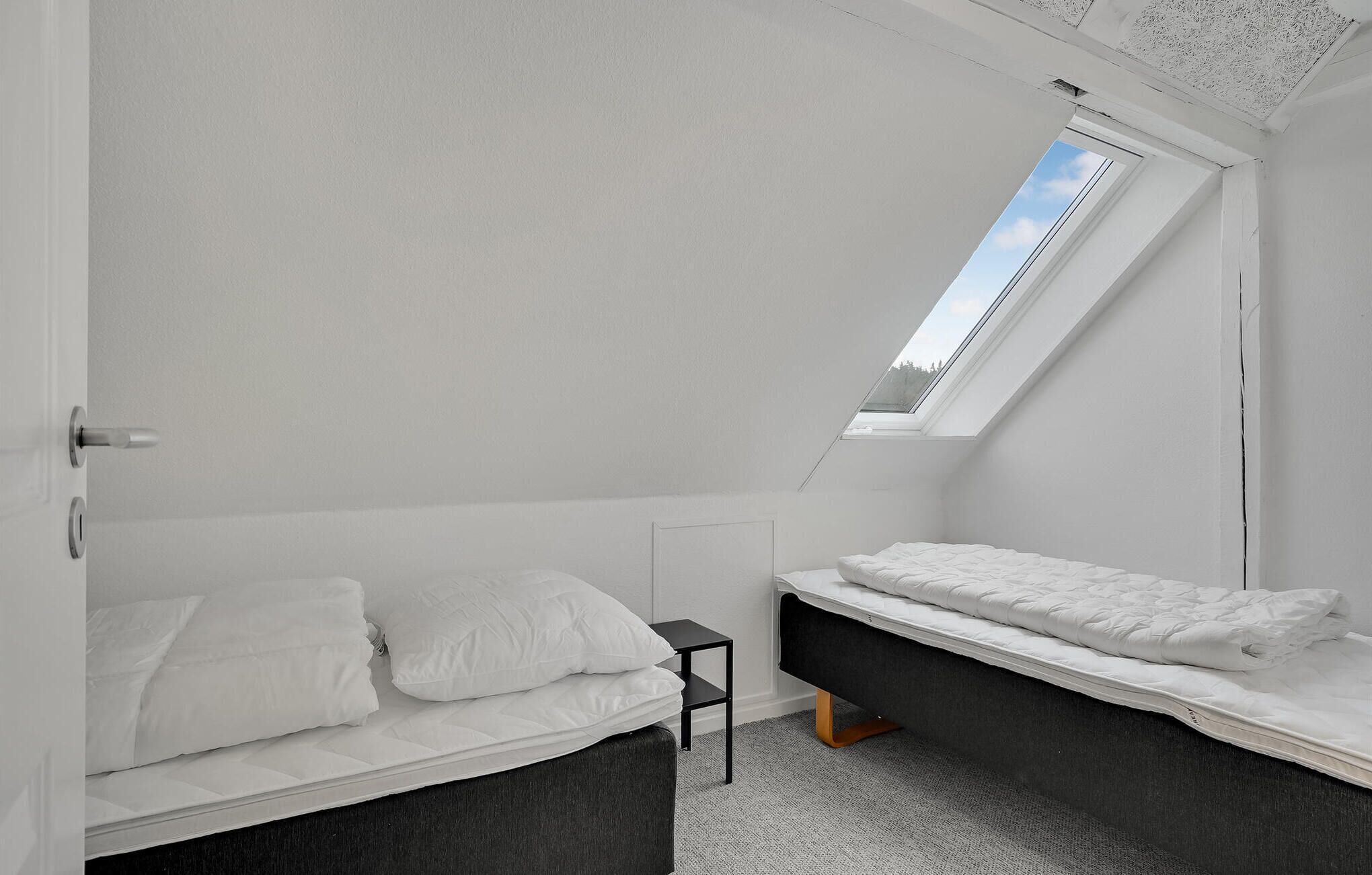 A bedroom with a skylight, two beds, a small table, and a carpeted floor.
