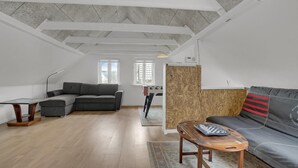A spacious living area with a grey sectional sofa, a wooden coffee table, and a wooden floor. There is a window with a view of trees and a ceiling with exposed beams. - 3 bedroom beautiful home in Bryrup (Bryrup)