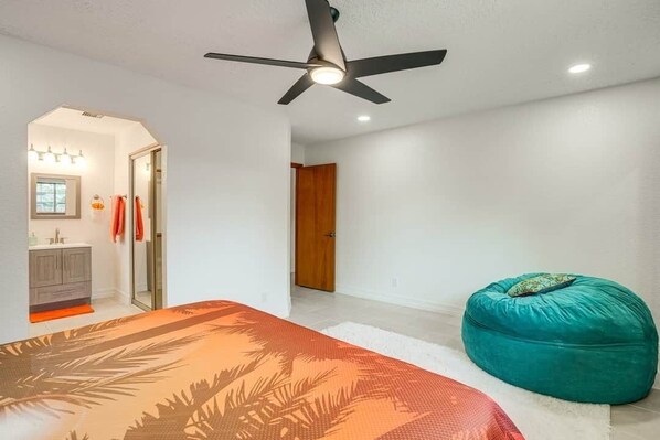 A bedroom with a bed, a ceiling fan, a teal bean bag, and a bathroom with a shower and a sink.