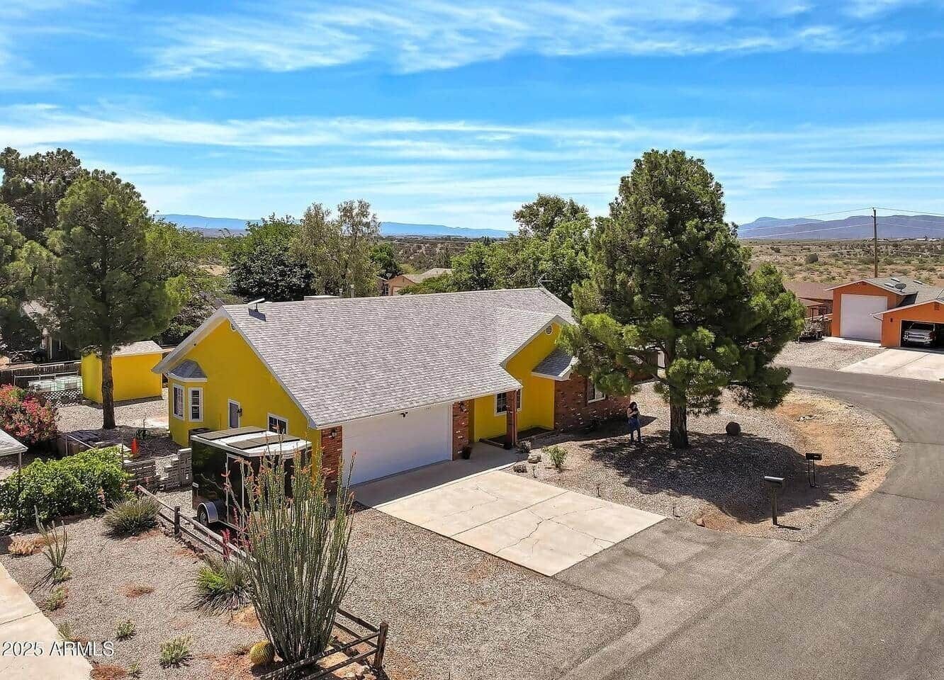 A yellow house with a garage, surrounded by trees and a clear sky.