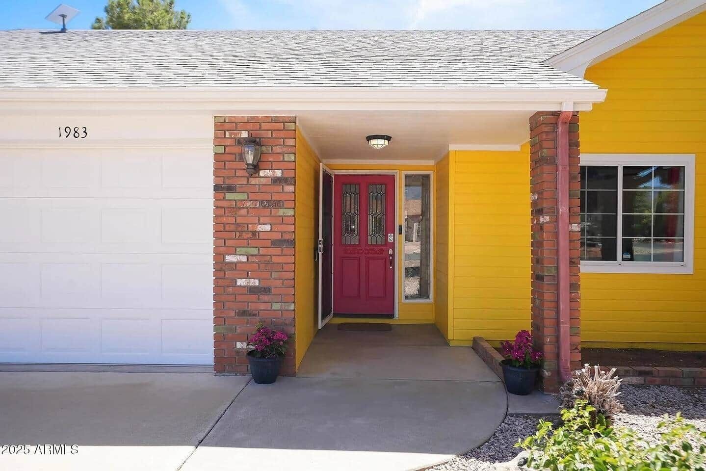 A yellow house with a red door, a garage, and a brick pillar.