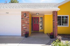 A yellow house with a red door, a garage, and a brick pillar.