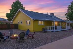 A yellow house with a porch, a fire pit, and outdoor seating.