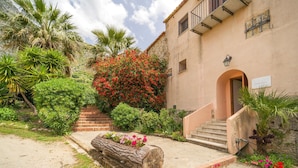 A building with a stone staircase leading to a door, surrounded by lush greenery and a large red flowering bush. - Cozy home in San Giuseppe Jato with swimming pool (San Giuseppe Jato)