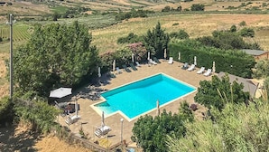 A rectangular swimming pool surrounded by lounge chairs and umbrellas, set against a backdrop of rolling hills and a distant town. - Cozy home in San Giuseppe Jato with swimming pool (San Giuseppe Jato)