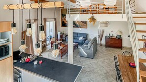 Un vaste espace de vie doté d’un haut plafond, un coin repas avec une table en bois et une cuisine avec un plan de travail noir.