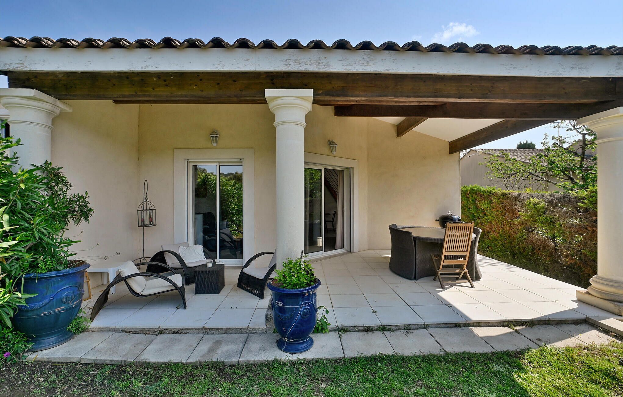 Un patio couvert avec des meubles d’extérieur, une porte-fenêtre coulissante et des plantes en pot.