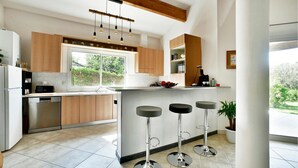 Une cuisine moderne avec des meubles en bois, un lave-vaisselle encastré, une grande fenêtre et trois tabourets de bar.