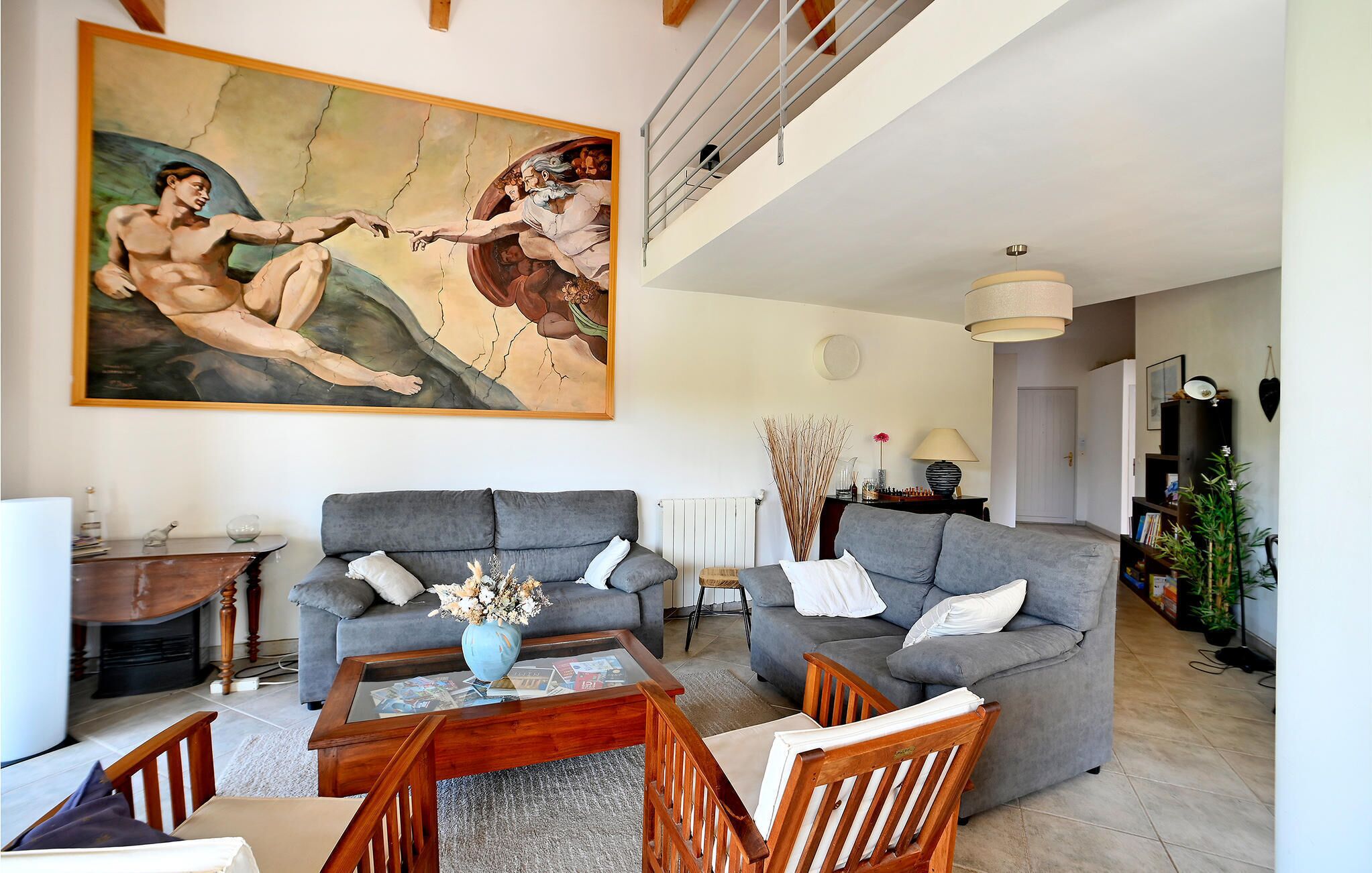 A spacious living room with a large painting, two grey sofas, a wooden coffee table, and a bookshelf.