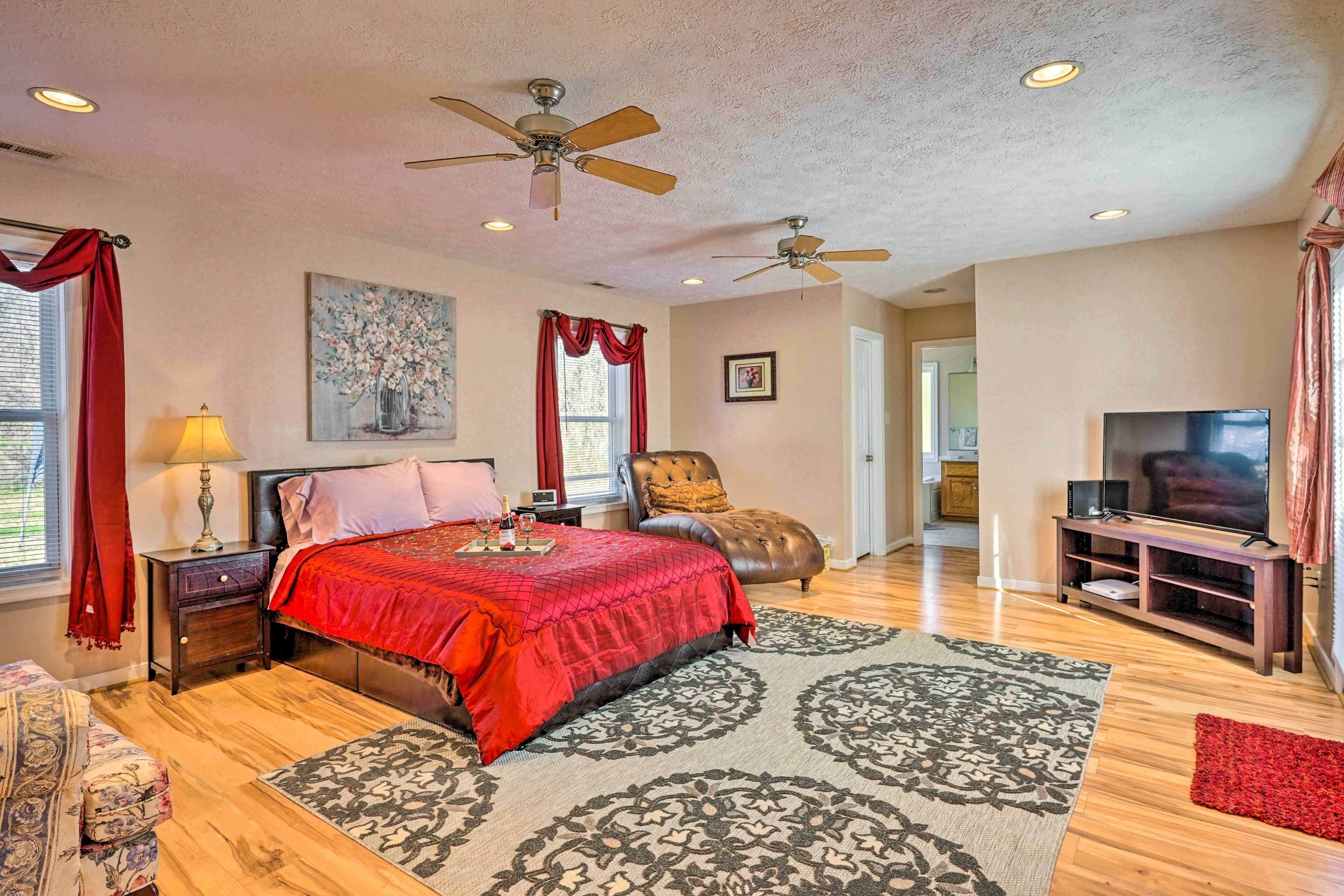 A spacious bedroom with a large bed, two ceiling fans, a TV, and a red accent wall.