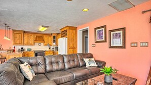 A living room with a brown leather sofa, a marble coffee table, and a kitchen in the background with wooden cabinets and a refrigerator.