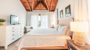 A bedroom with a wooden ceiling, a bed with white bedding, a bedside table with a lamp, a TV on a dresser, and a window with curtains. - Ocean View Villa with Pool & BBQ in Samana (Samaná)