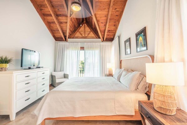 A bedroom with a wooden ceiling, a bed with white bedding, a bedside table with a lamp, a TV on a dresser, and a window with curtains.