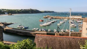 A harbor with boats docked, a stone wall, and a building with a red roof. - Bluebell Cottage (Tenby)