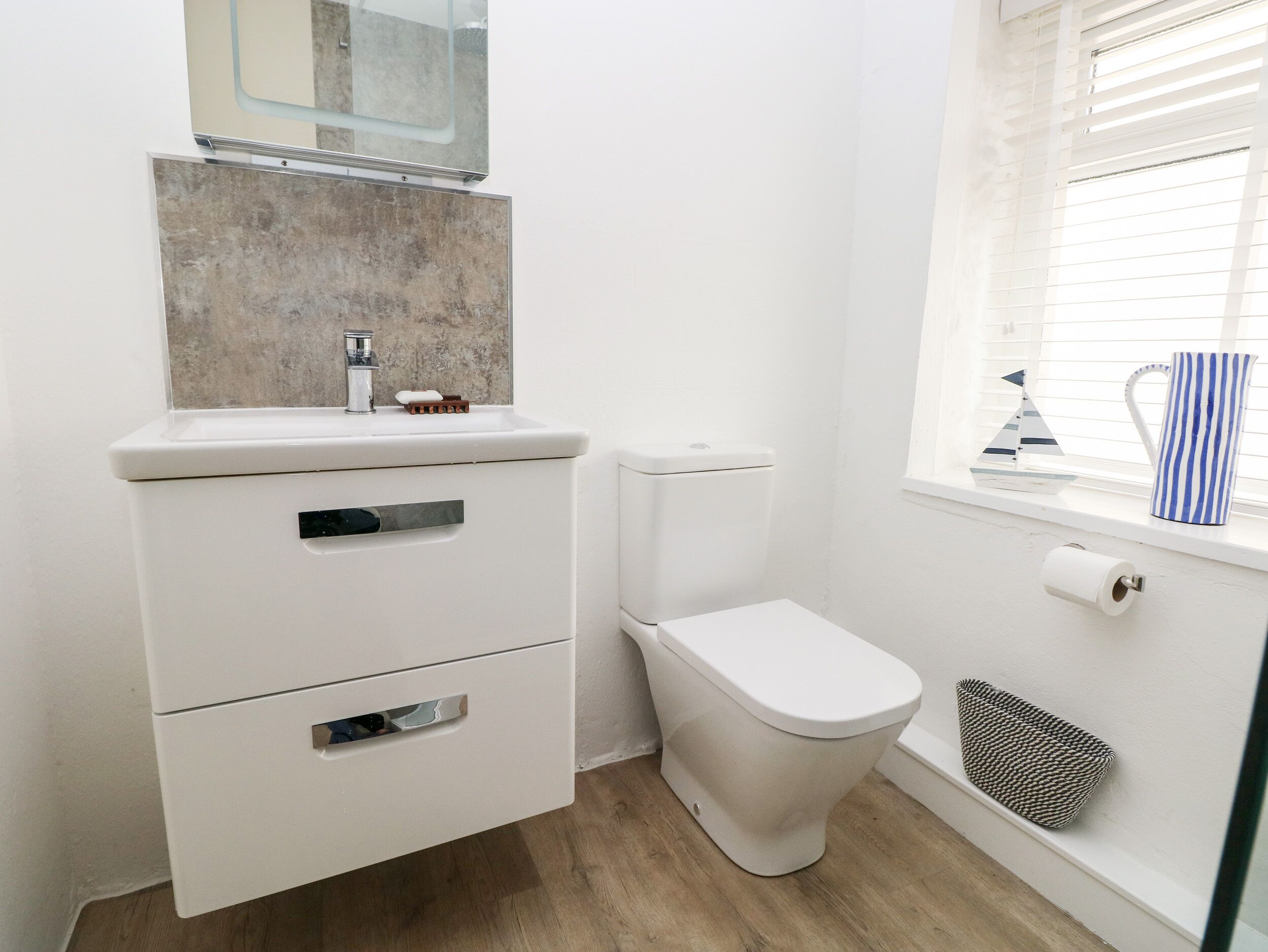 Een kleine badkamer met toilet, een wastafel met spiegel, en een raam met zonwering.