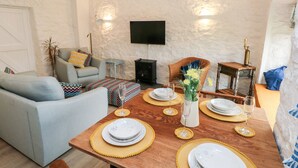 A cozy living room with a sofa, a dining table set with plates and glasses, and a fireplace. - Bluebell Cottage (Tenby)