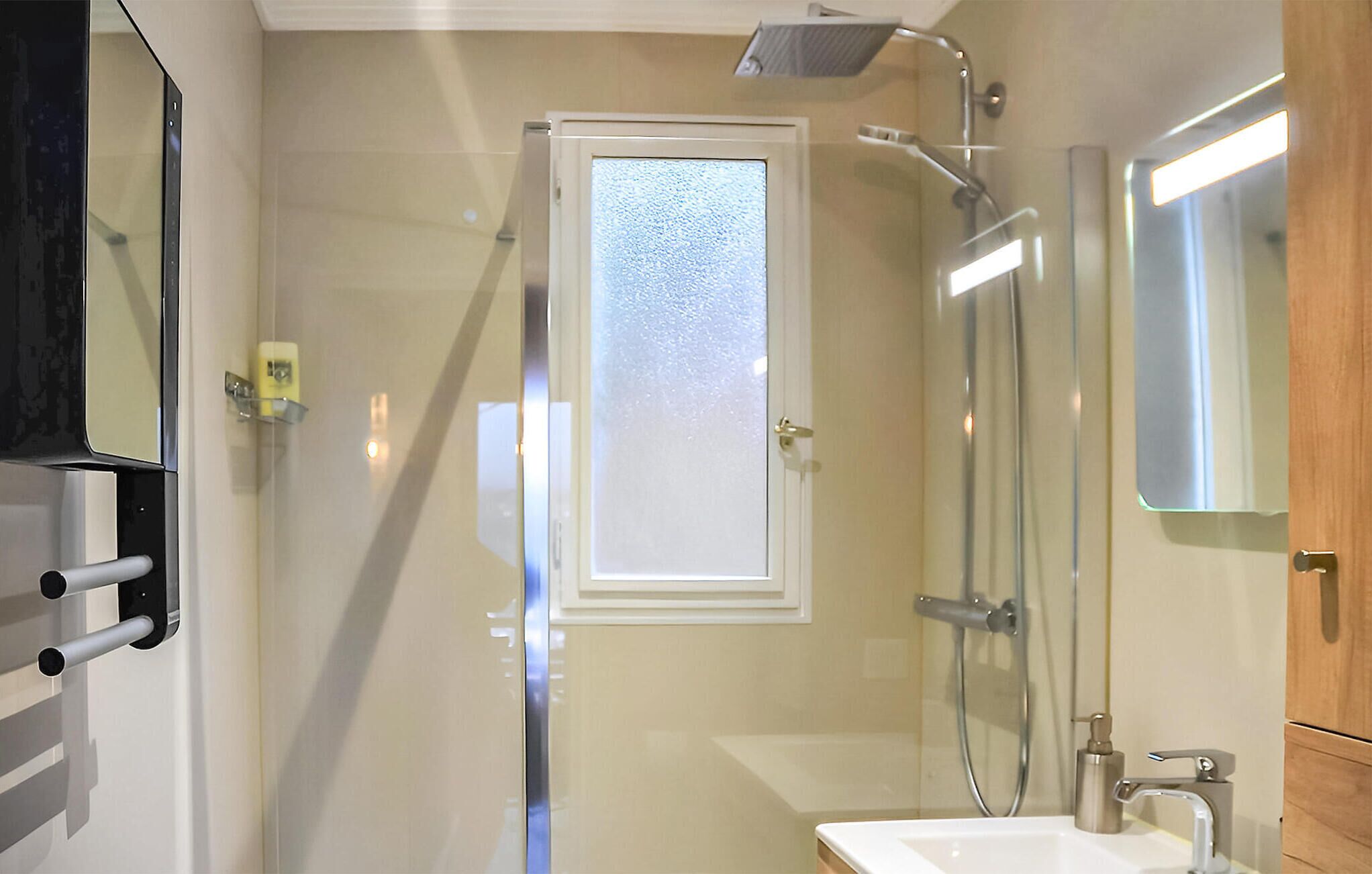 A modern bathroom with a glass shower enclosure, a sink, and a mirror.