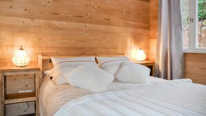 A wooden cabin bedroom with a bed, two bedside lamps, and a window with curtains. - Lovely apartment in Gérardmer with house sea view (Gérardmer)