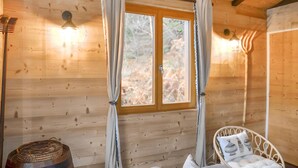 A wooden cabin room with a large window, a bed with a white headboard, and a small table with a basket. - Lovely apartment in Gérardmer with house sea view (Gérardmer)