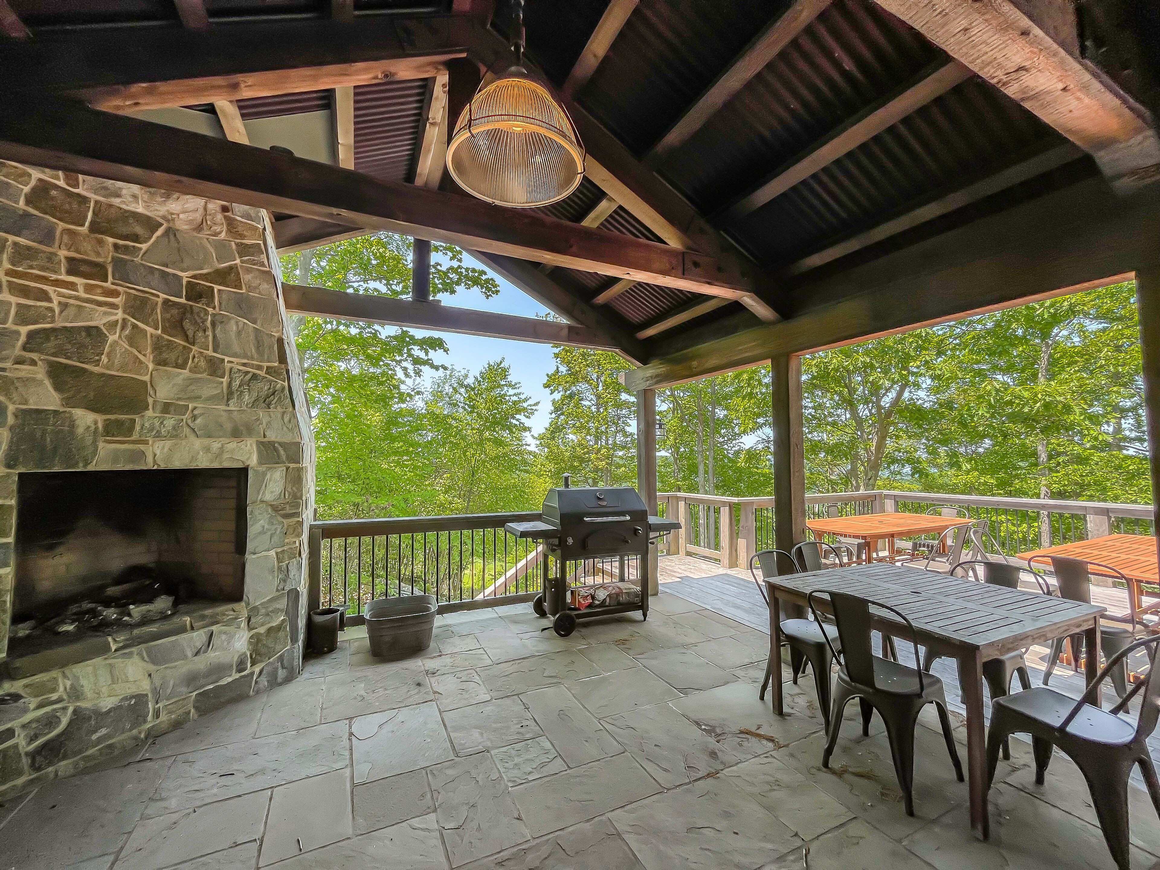 Un patio cubierto con muros de piedra, chimenea, mobiliario exterior y vistas a árboles.