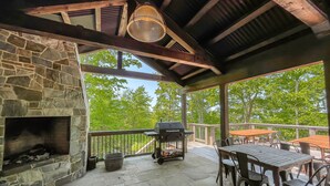 A covered patio with stone walls, a fireplace, outdoor furniture, and a view of trees.