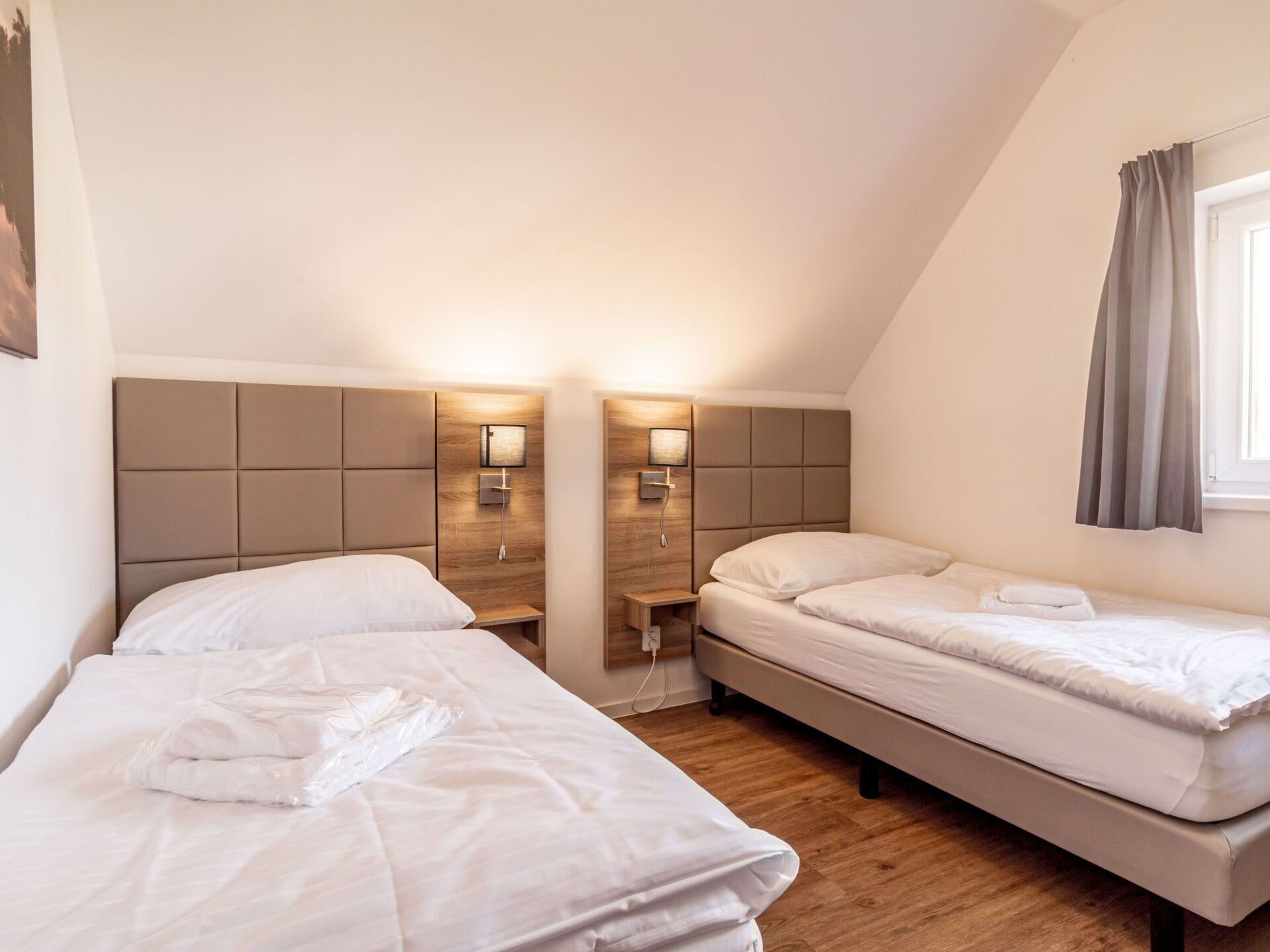 A room with two beds, each with a headboard and bedside tables. There are wall-mounted lamps on the headboards.
