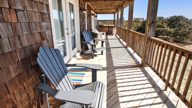 Eine Holzterrasse mit Adirondack-Stühlen und einem Tisch, mit Blick auf eine Wohngegend.