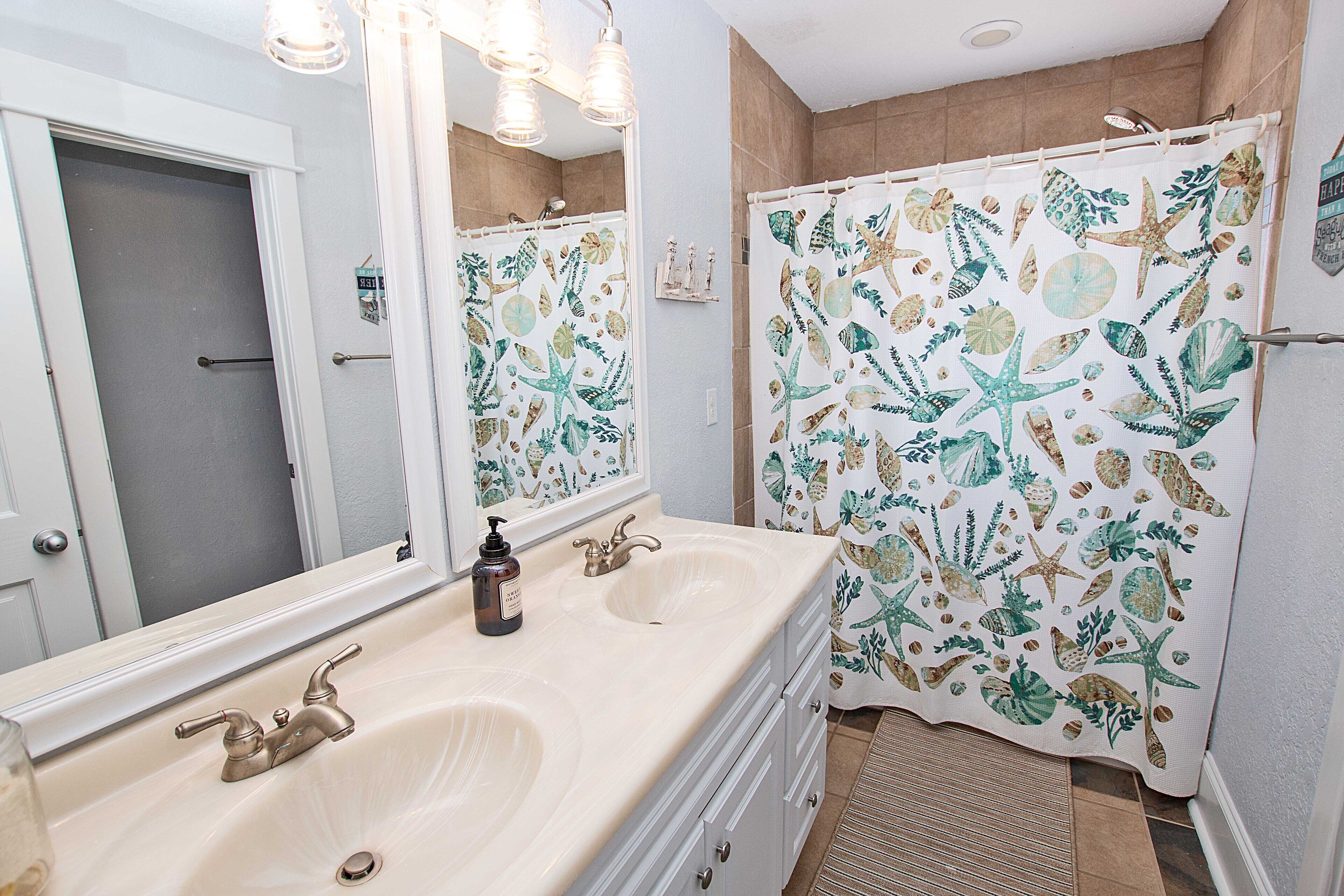Une salle de bain avec un double lavabo, un grand miroir et un rideau de douche orné d’un motif sur le thème de la mer.