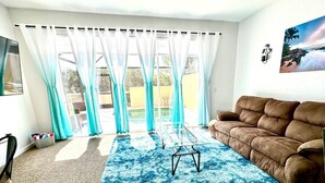 A living room with a brown sofa, a glass coffee table, and a blue patterned rug. - Free Water Park! August on Sale Now! (Kissimmee)