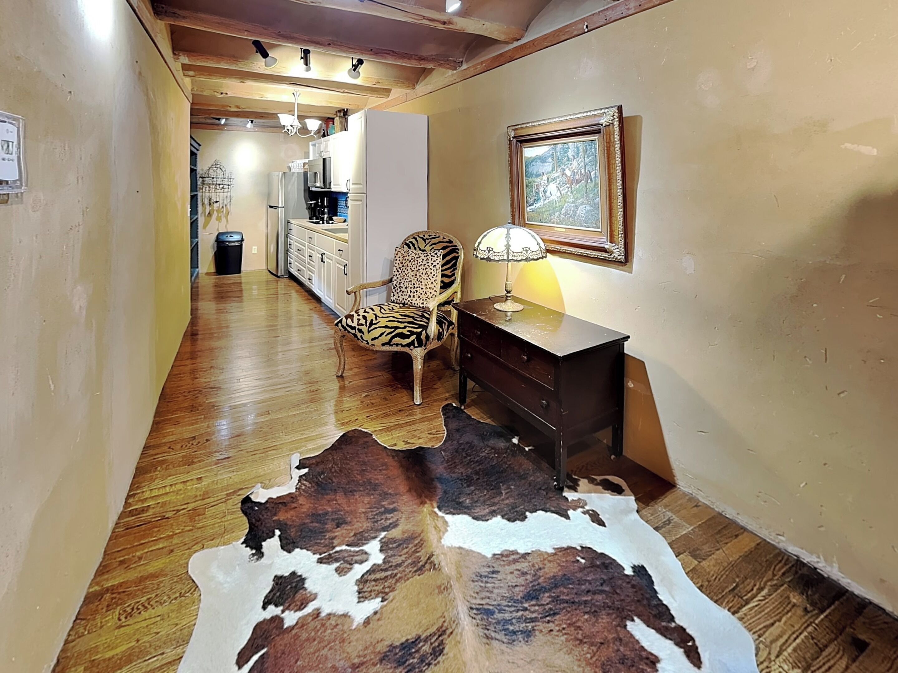 A hallway with wooden flooring, a zebra-patterned chair, a lamp, a framed picture, and a cowhide rug.