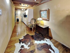 Um corredor com piso de madeira, uma cadeira estampada em zebra, um abajur, um quadro emoldurado e um tapete de couro de vaca.