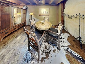 A rustic dining area with a round wooden table, four chairs with wooden frames, a cowhide rug, and a wooden cabinet with a mirror and lamps. - Casita Mariposa by Kokopelli Property Management (Santa Fe)