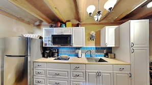 Cocina compacta con armarios blancos, un refrigerador de acero inoxidable, microondas y cafetera.